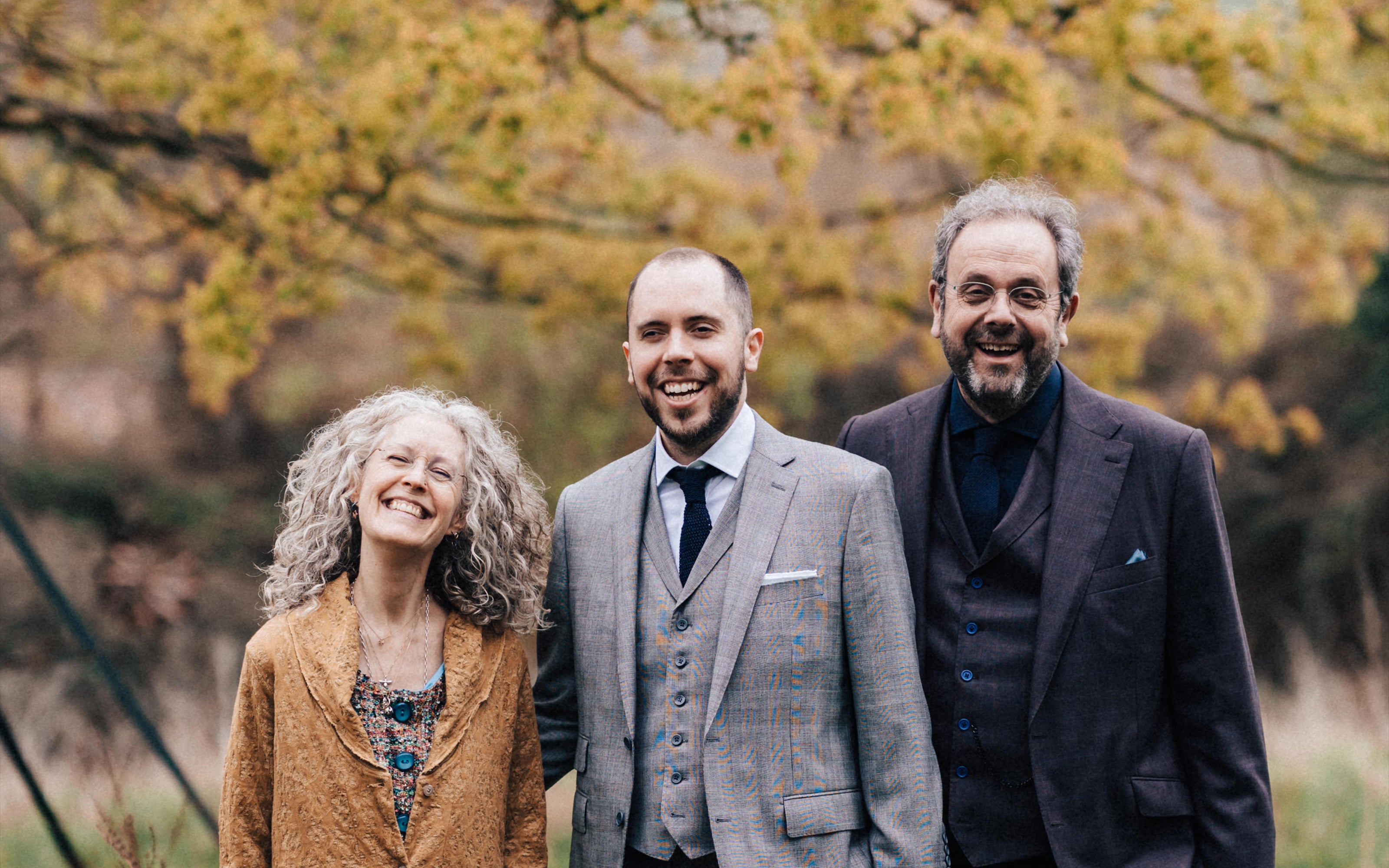 Be, Tim and Drew Montague standing together outdoors under an autumn tree